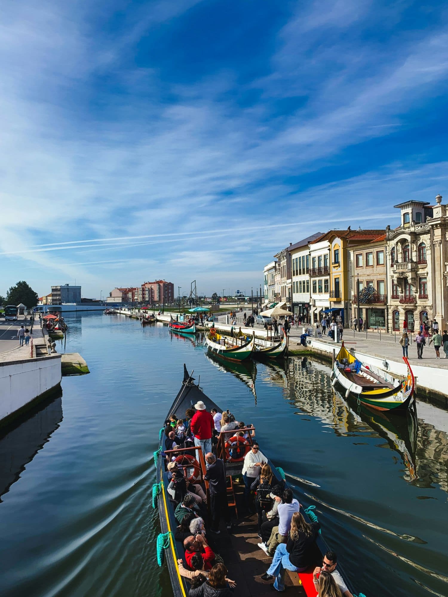 A moliceiro full of passengers heading down Aveiro’s central canal, with painted boats moored along the quay