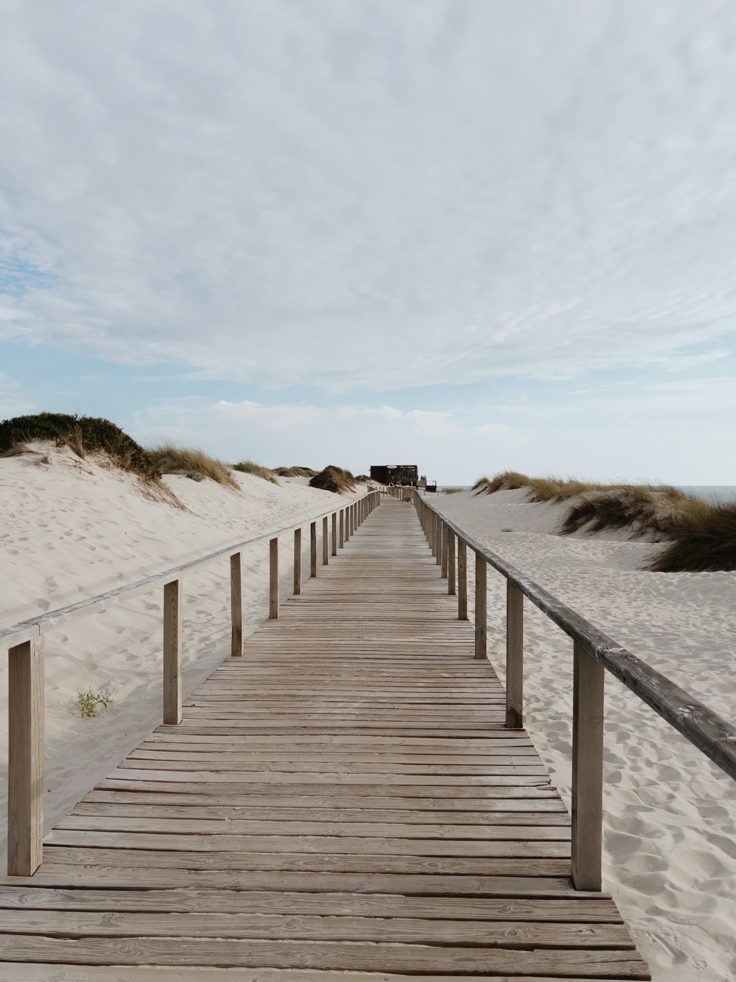 A boardwalk running between grassy dunes towards the sea