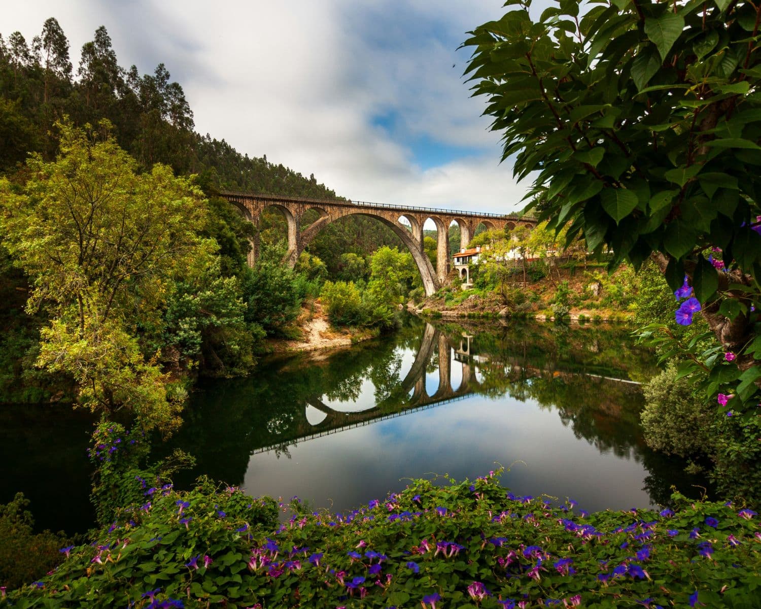 The arched stone railway bridge over the Vouga river, reflected in the still river